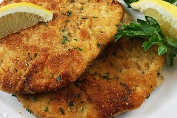 close up view of Chicken Milanese with lemon wedges and herbs